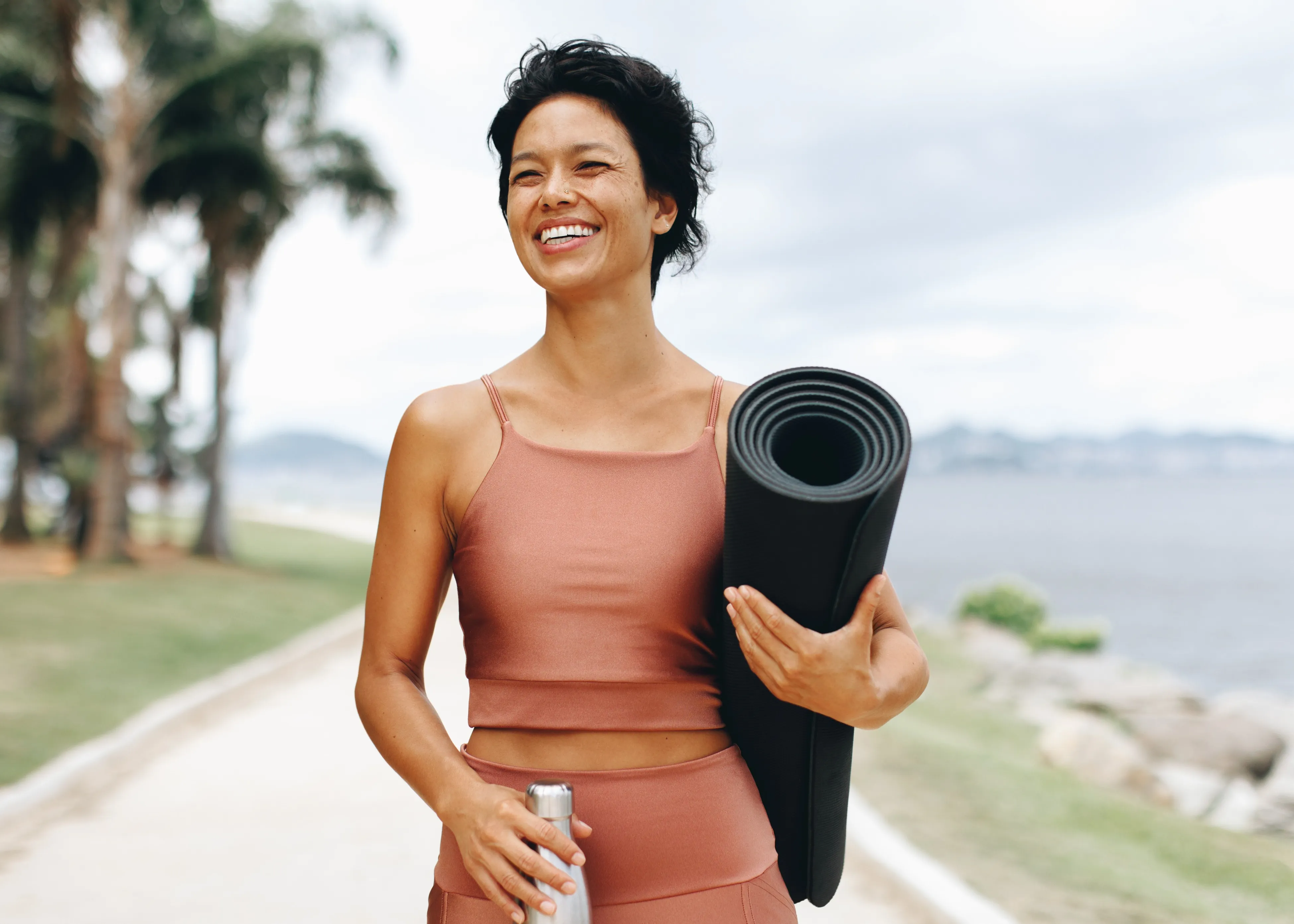 A woman holding a yoga mat and smiling.