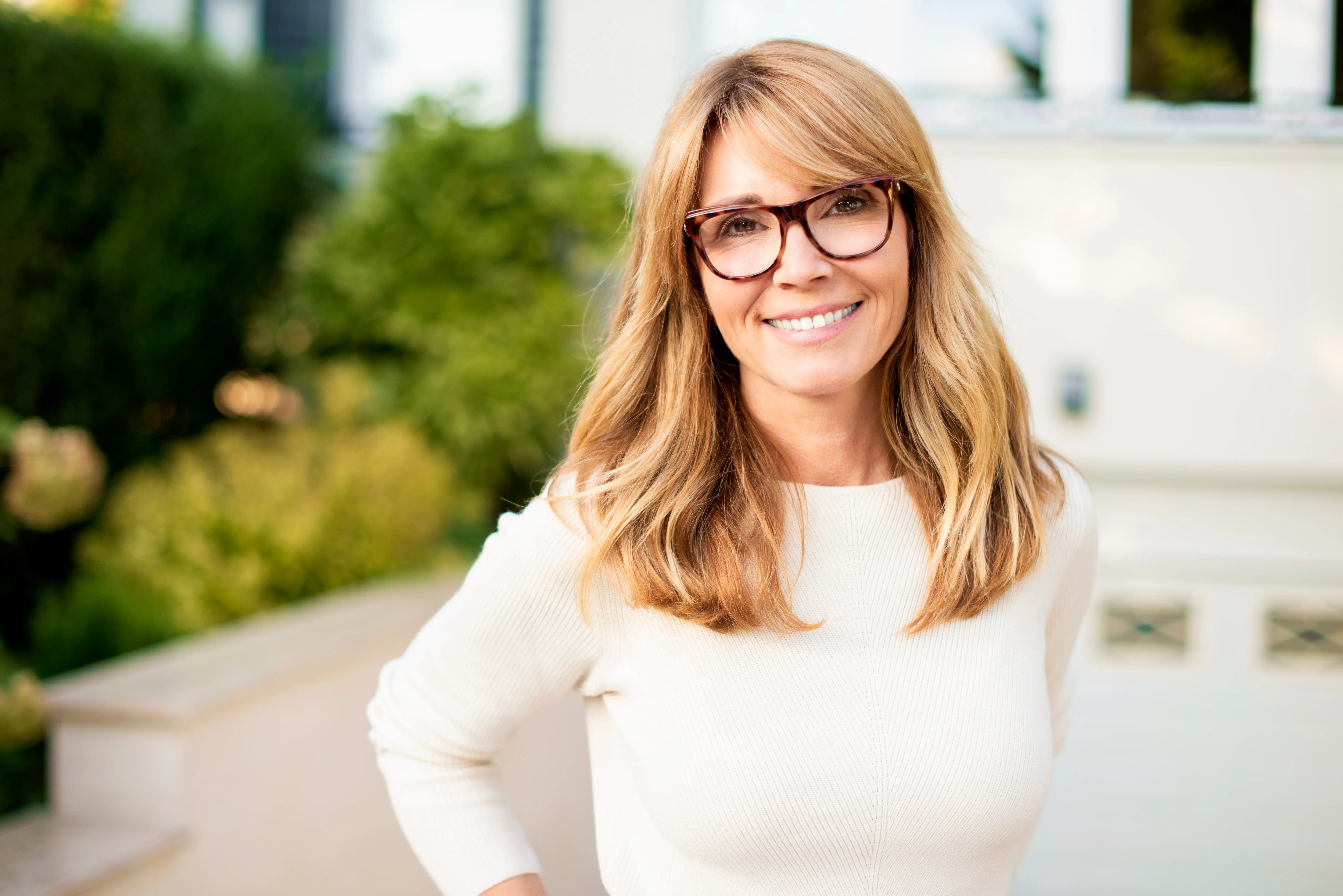 A woman wearing glasses standing in front of a building.