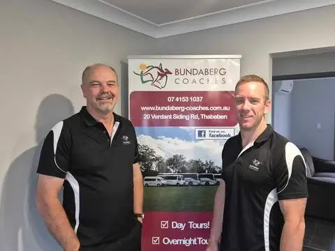 Staff members of Bundaberg Coaches in uniform, standing in front of a pull-up banner for their business