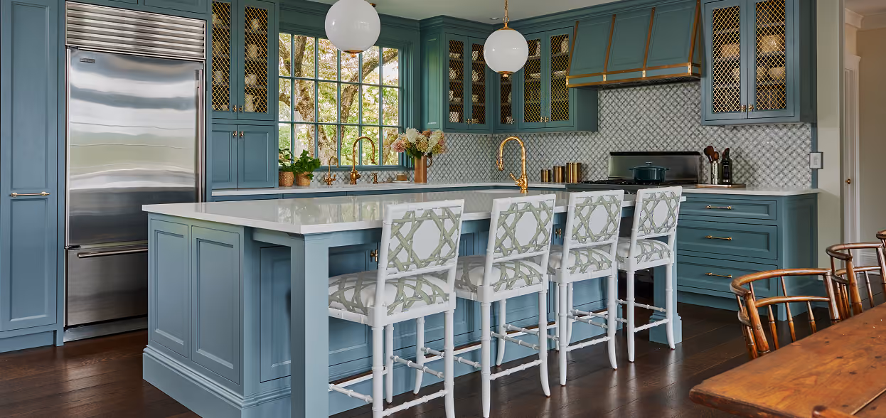A spacious kitchen with muted blue-gray cabinetry, a large kitchen island with patterned barstools, and stainless steel appliances