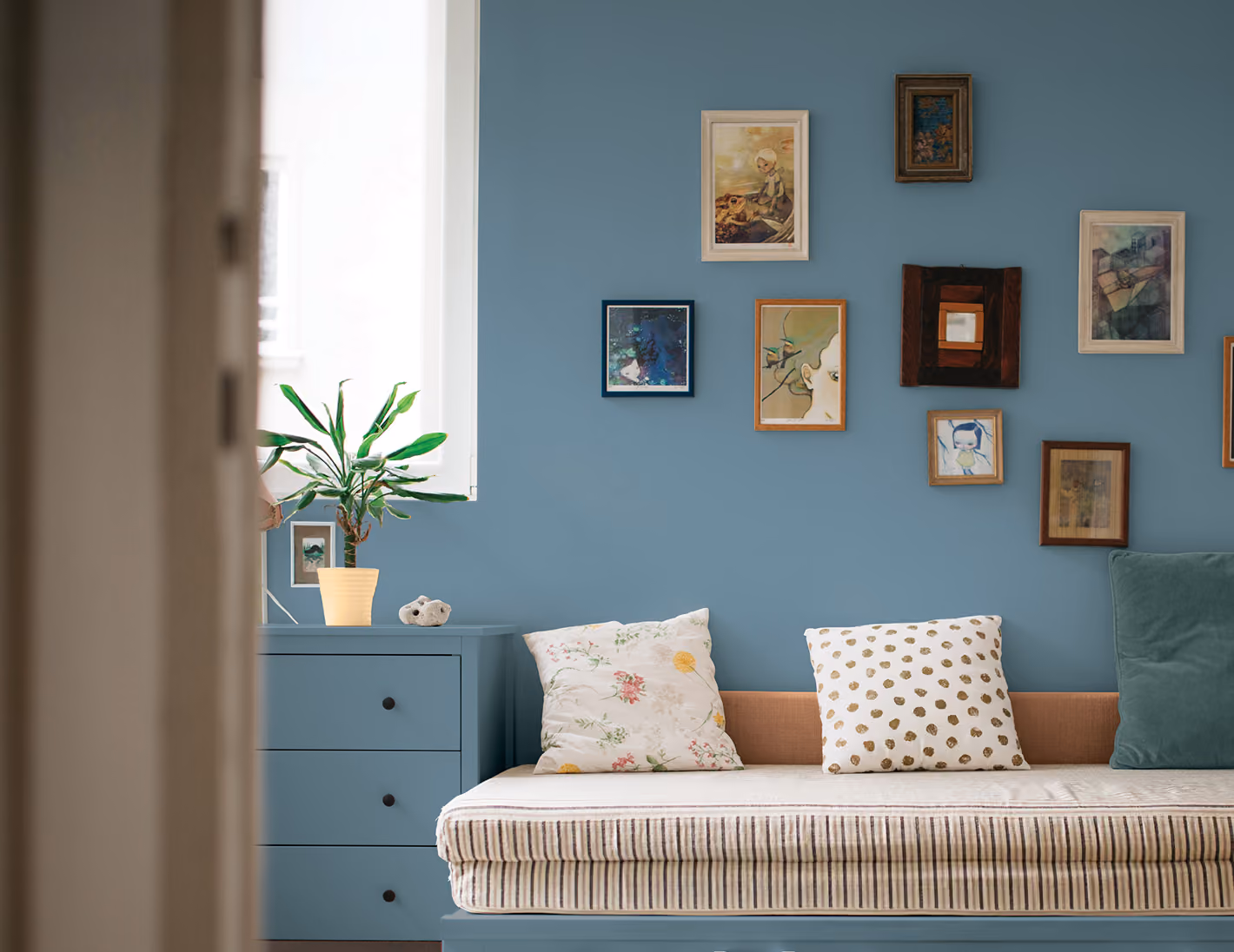 A cozy daybed and blue dresser against a blue wall with framed pictures