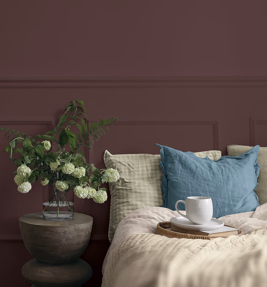 A cozy bed and flowers against a dark plum painted wall