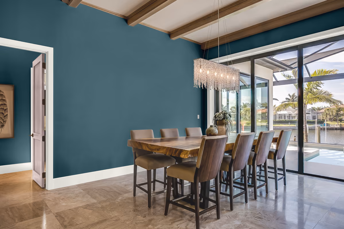 Modern dining room with a rich teal accent wall and a long wooden table next to glass doors