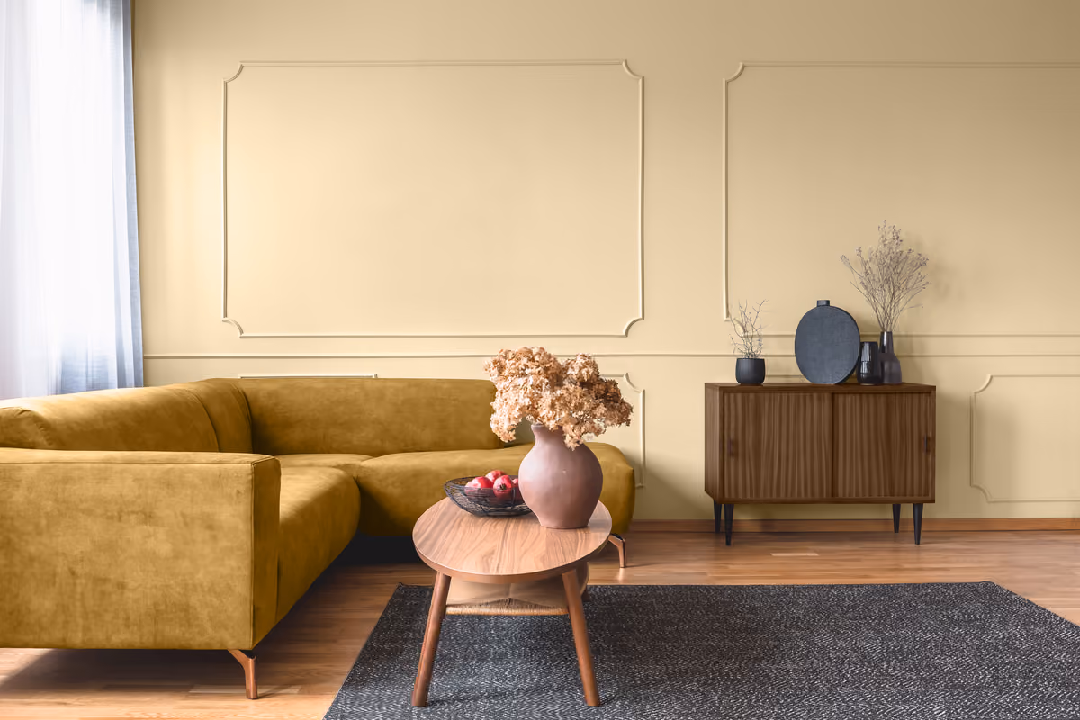Warm, cream-colored living room featuring a mustard yellow sectional sofa and dark wood cabinet