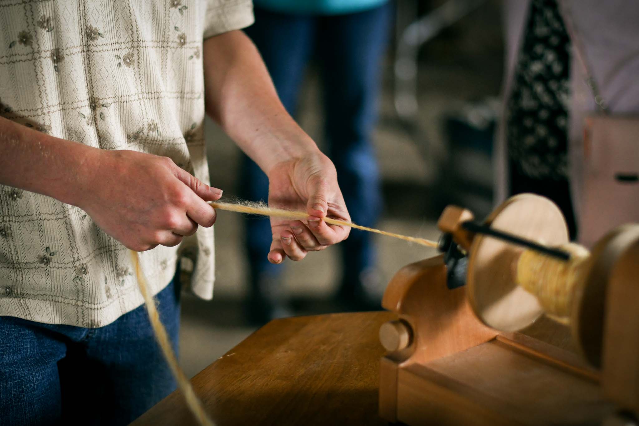 Person spinning yarn by hand using a wooden spinning wheel.