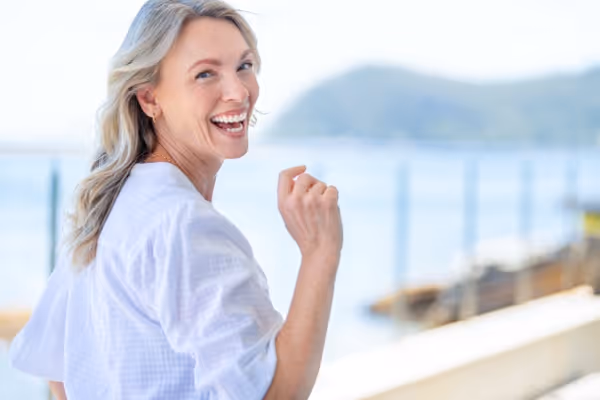 A woman walking along the coastline, smiling and looking back at the camera, radiating happiness and enjoying a vibrant, active lifestyle.