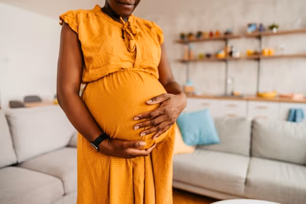Pregnant woman standing in a living room, lovingly caressing her belly and expressing maternal affection and anticipation.