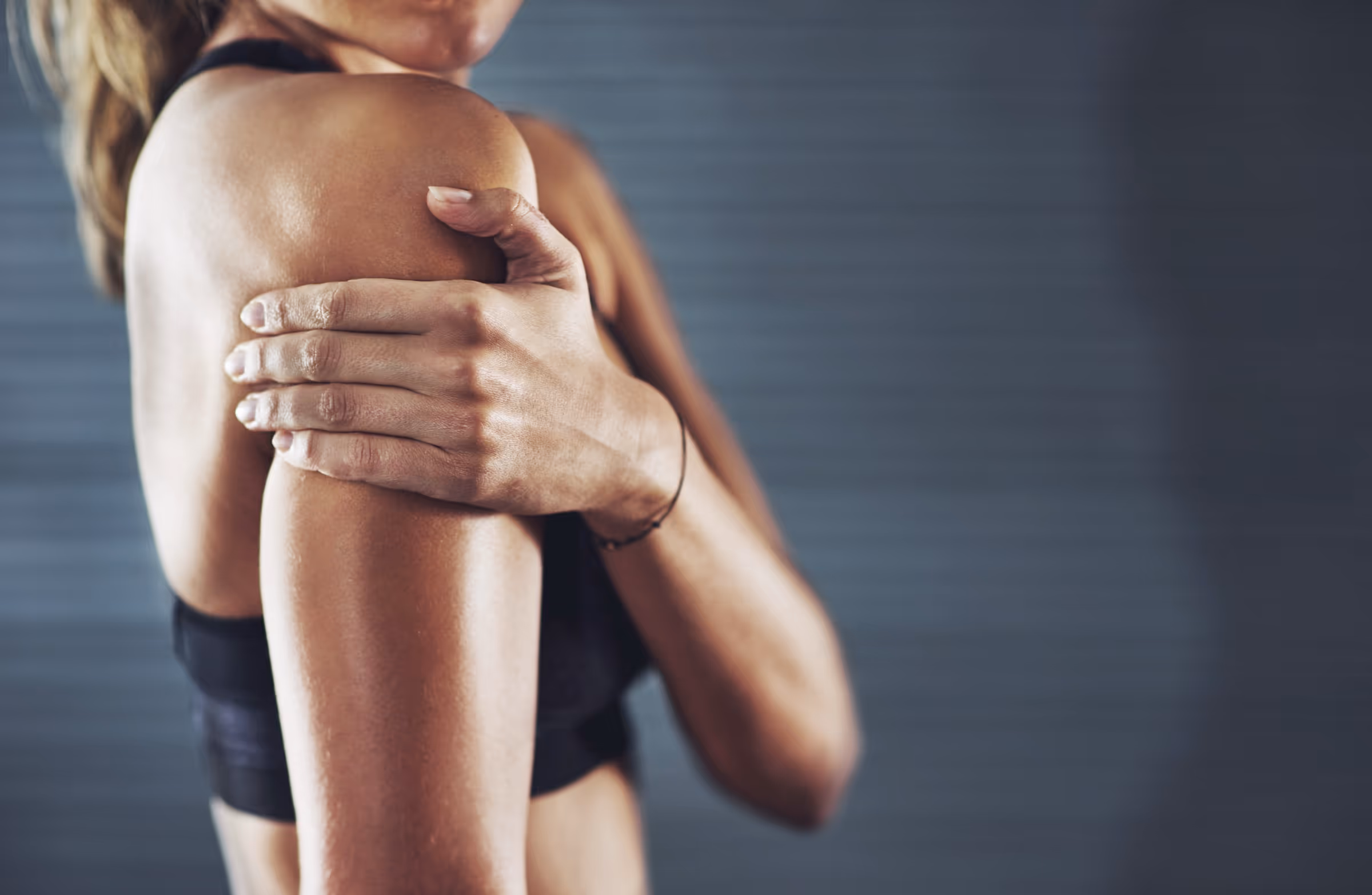Woman holding her shoulder in pain while wearing exercise clothes, highlighting how chronic pain can disrupt daily activities and quality of life