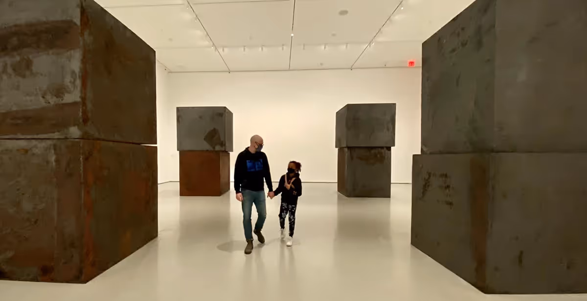 A father and daughter walking between several large blocks of stone in a room