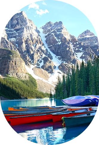 Colorful canoes docked on a clear blue lake surrounded by green pine trees and snow-capped mountains under a blue sky.