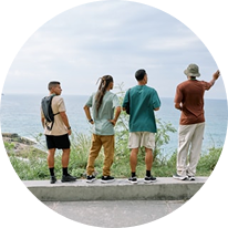 Four people standing on a ledge facing the ocean, with one pointing into the distance.
