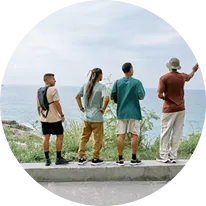 Four people standing on a ledge facing the ocean, with one pointing into the distance.
