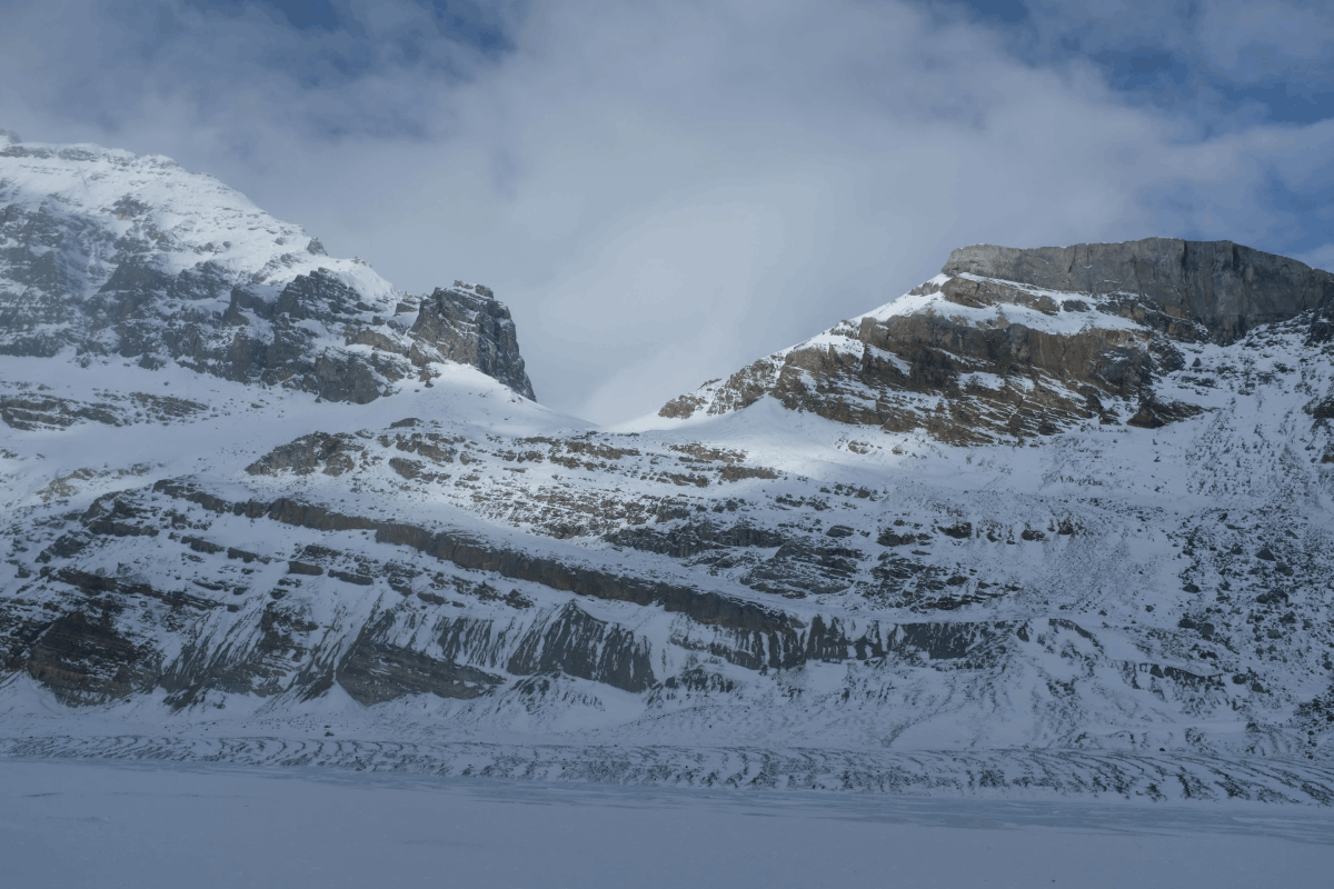 Snow-covered rocky mountain peaks under a cloudy sky.