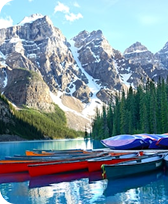 Red and blue kayaks docked on a calm lake with tall evergreen trees and snow-capped mountains in the background.