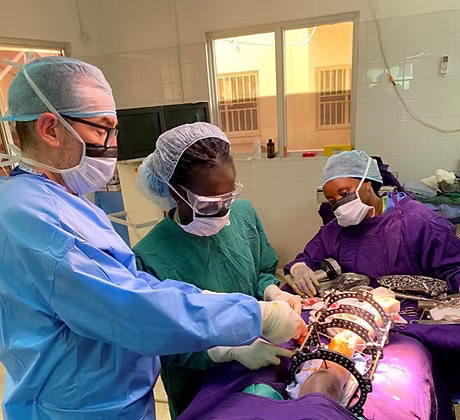 Three surgeons perform surgery in an operating room, wearing protective clothing and masks.