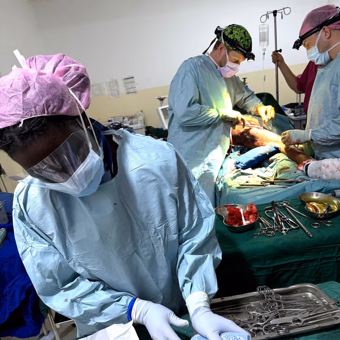 Doctors in surgical attire perform a medical procedure on a patient in an operating room.
