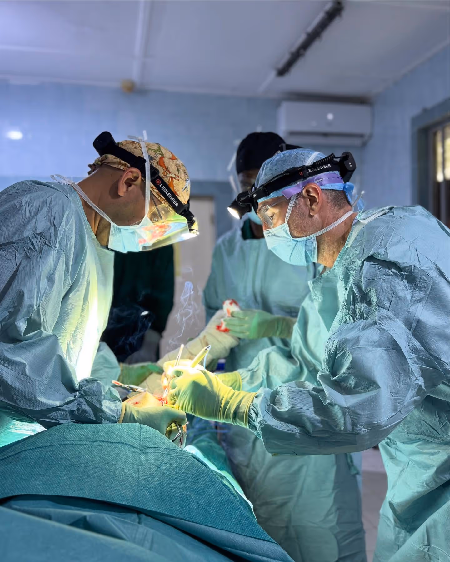 Doctors in surgical gowns and masks performing an operation under bright lights.