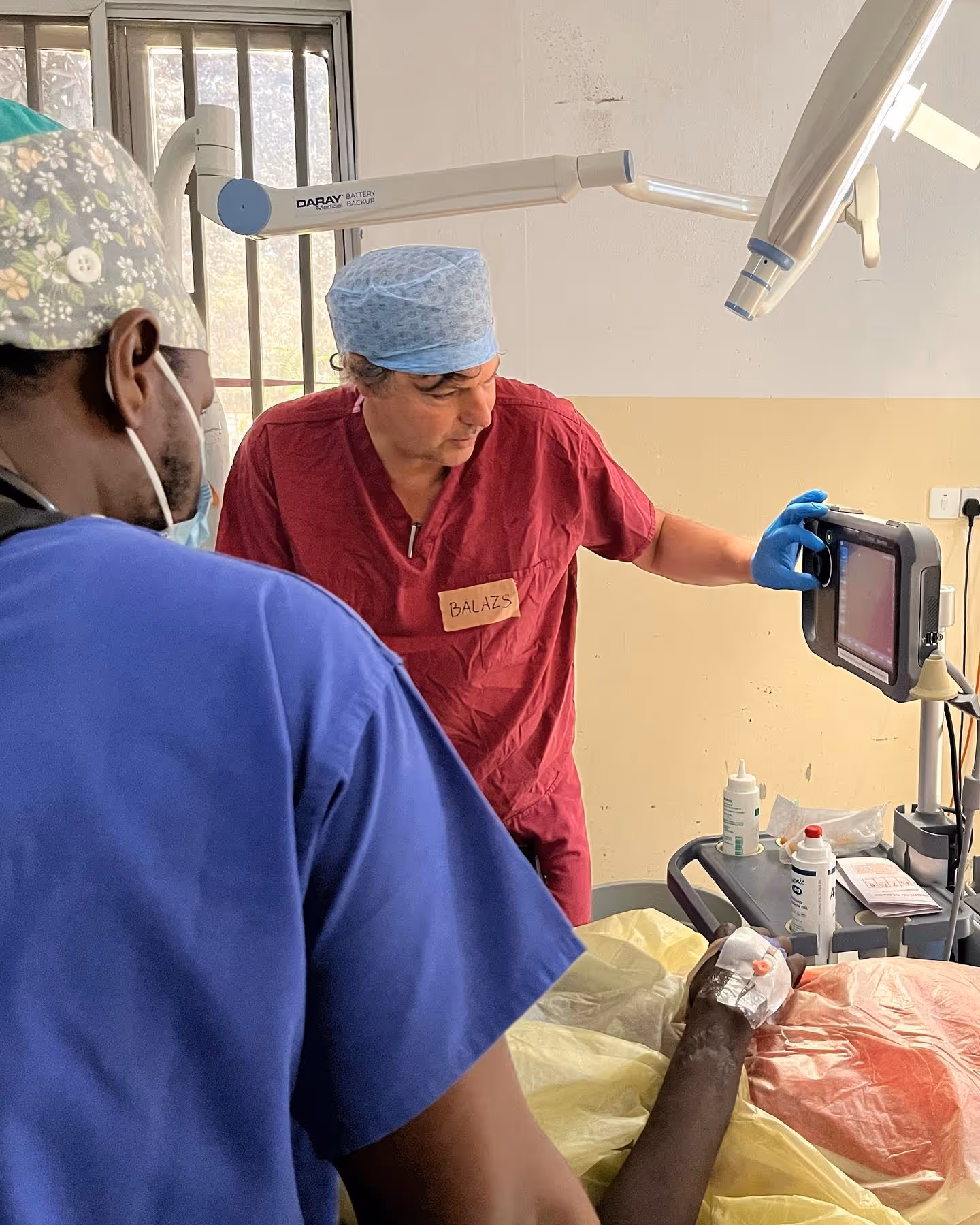 Two medical professionals examine an X-ray on a screen next to a patient in an operating room.