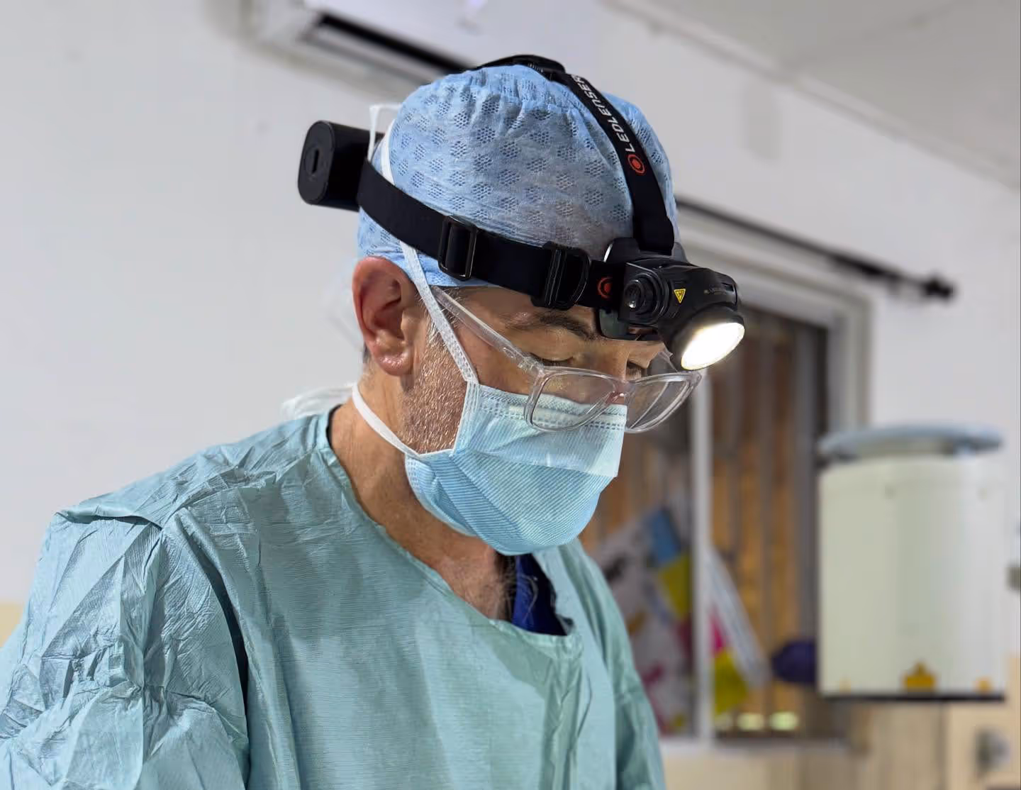 Surgeon wearing surgical attire and a headlamp, focused on performing a procedure.