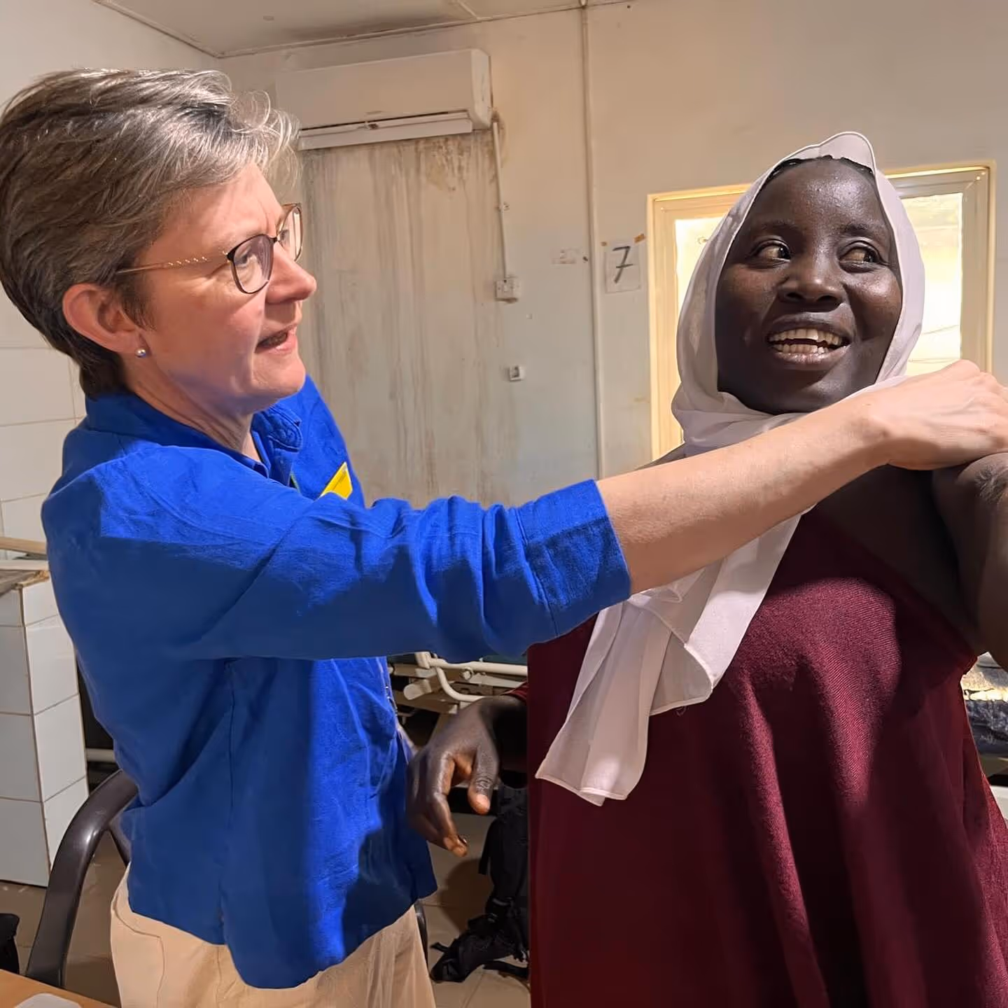 An older woman is assisting a younger woman with a medical check-up in a clinic.