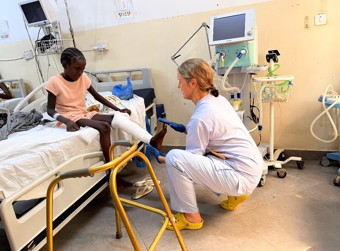 A healthcare worker checks a child's leg cast in a hospital room.