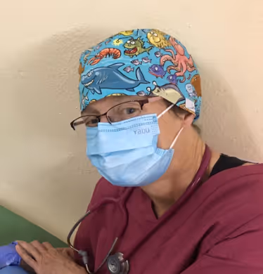 A healthcare worker in scrubs and a colorful cap wearing a mask and glasses.