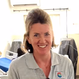 A woman wearing a light-colored polo shirt smiles in an indoor setting.