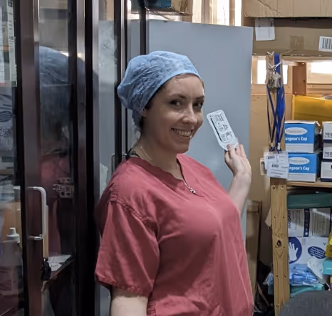 Person in a red shirt and blue cap smiling while opening a door in a storage room.