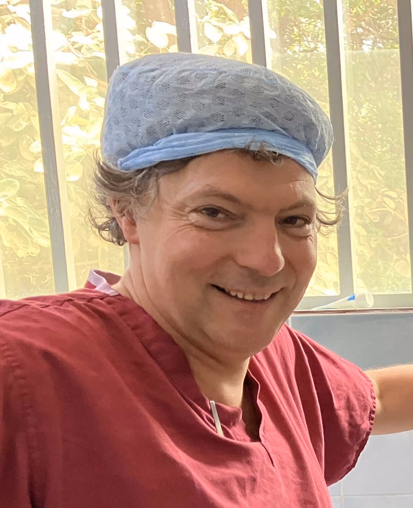 Person wearing a blue surgical cap and red scrubs, smiling in an indoor setting.
