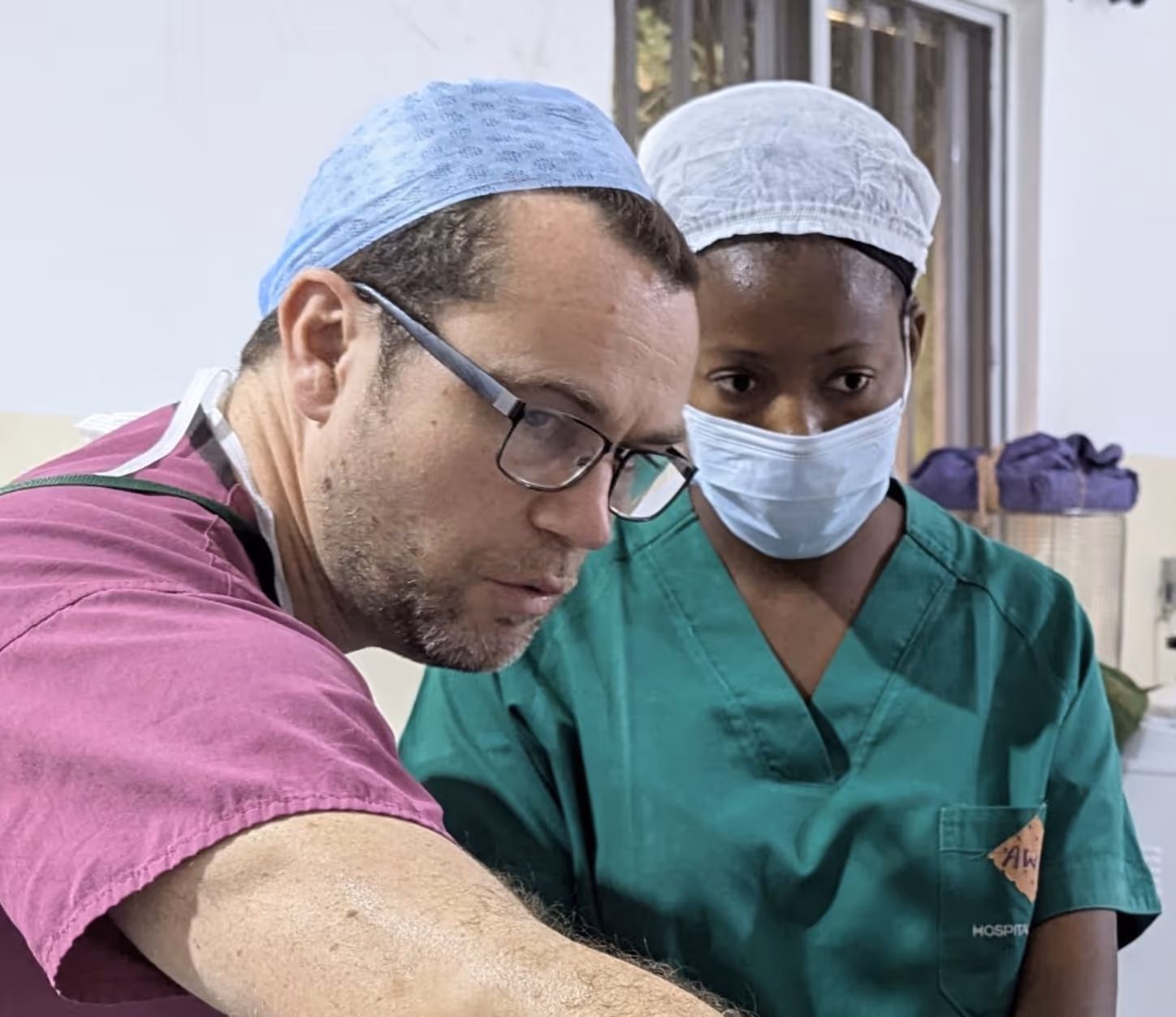 Two medical professionals in surgical attire focus on a task in a hospital setting.