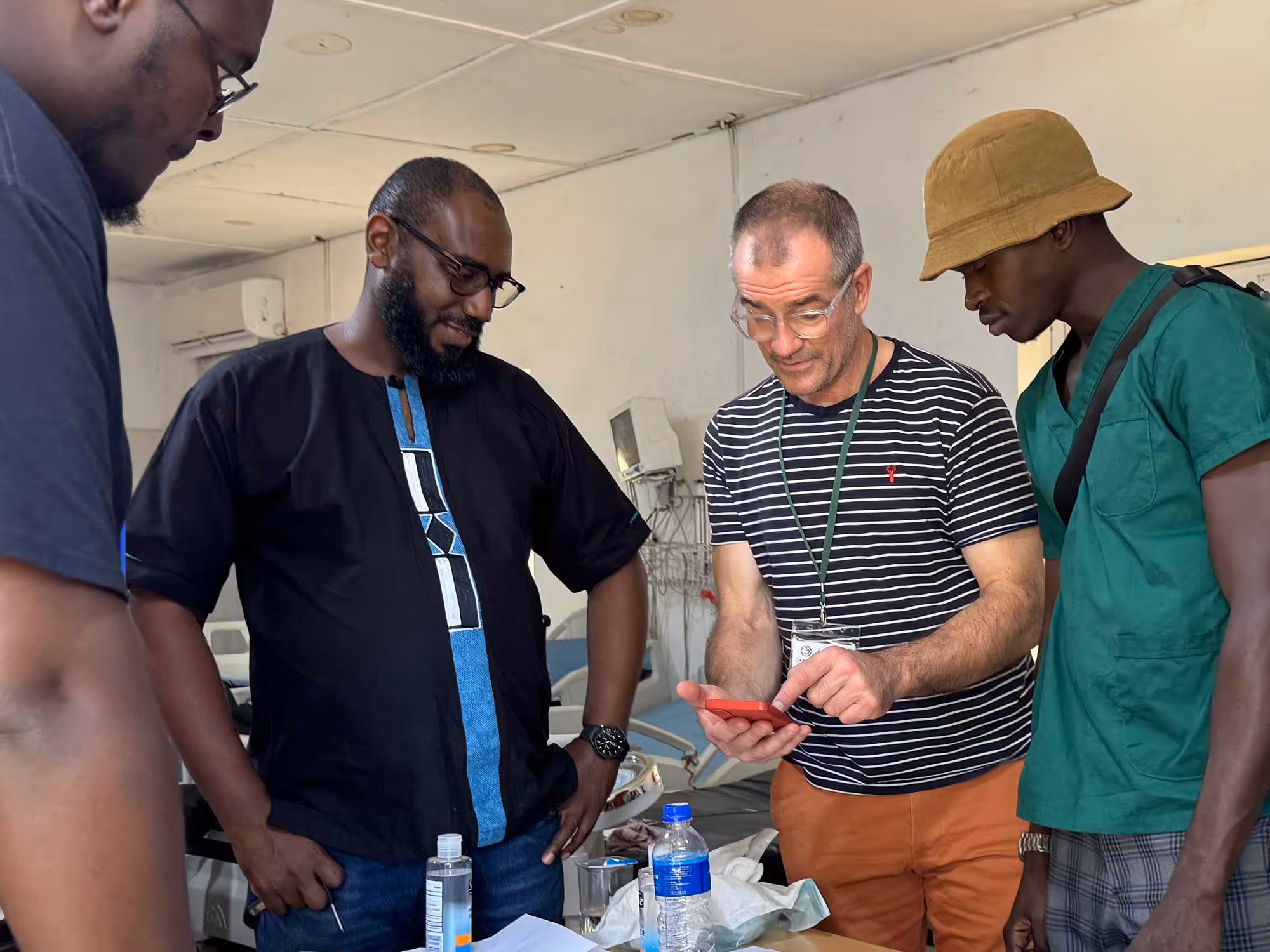 Four men standing together, one holding a red phone, discussing something intently.