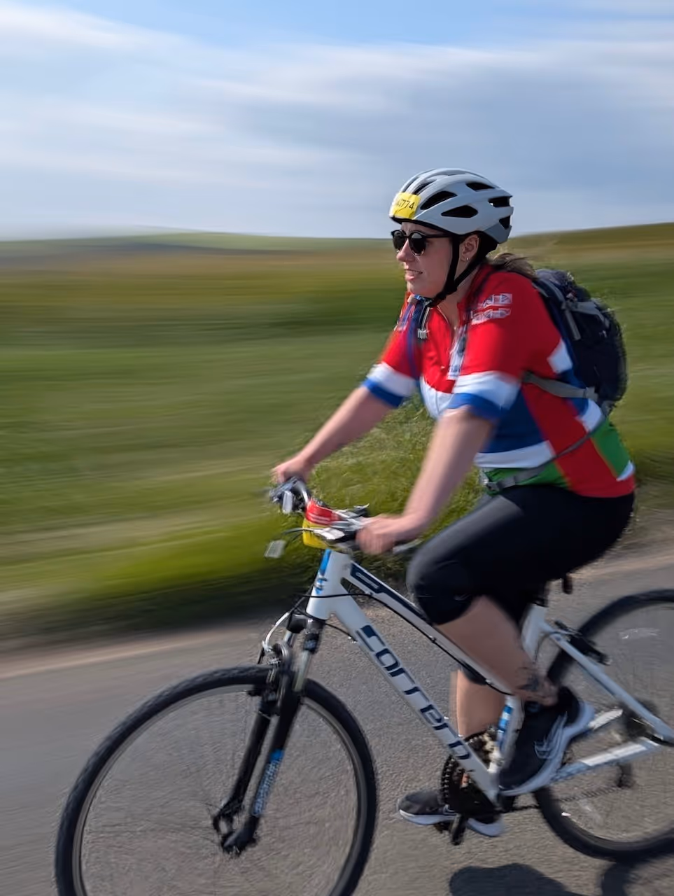 Person riding a bicycle on a road wearing a helmet and a colorful cycling jersey.