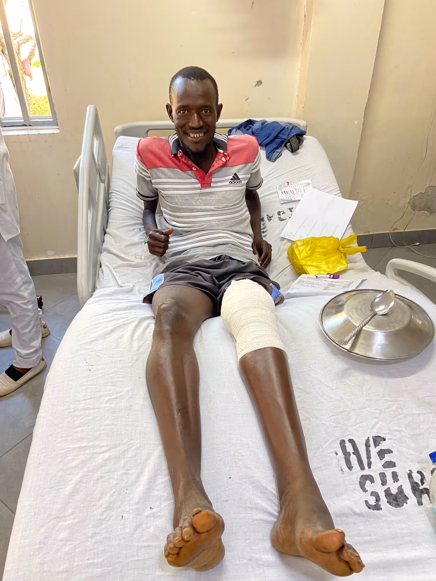 Man smiling while sitting on a hospital bed with a bandaged knee.