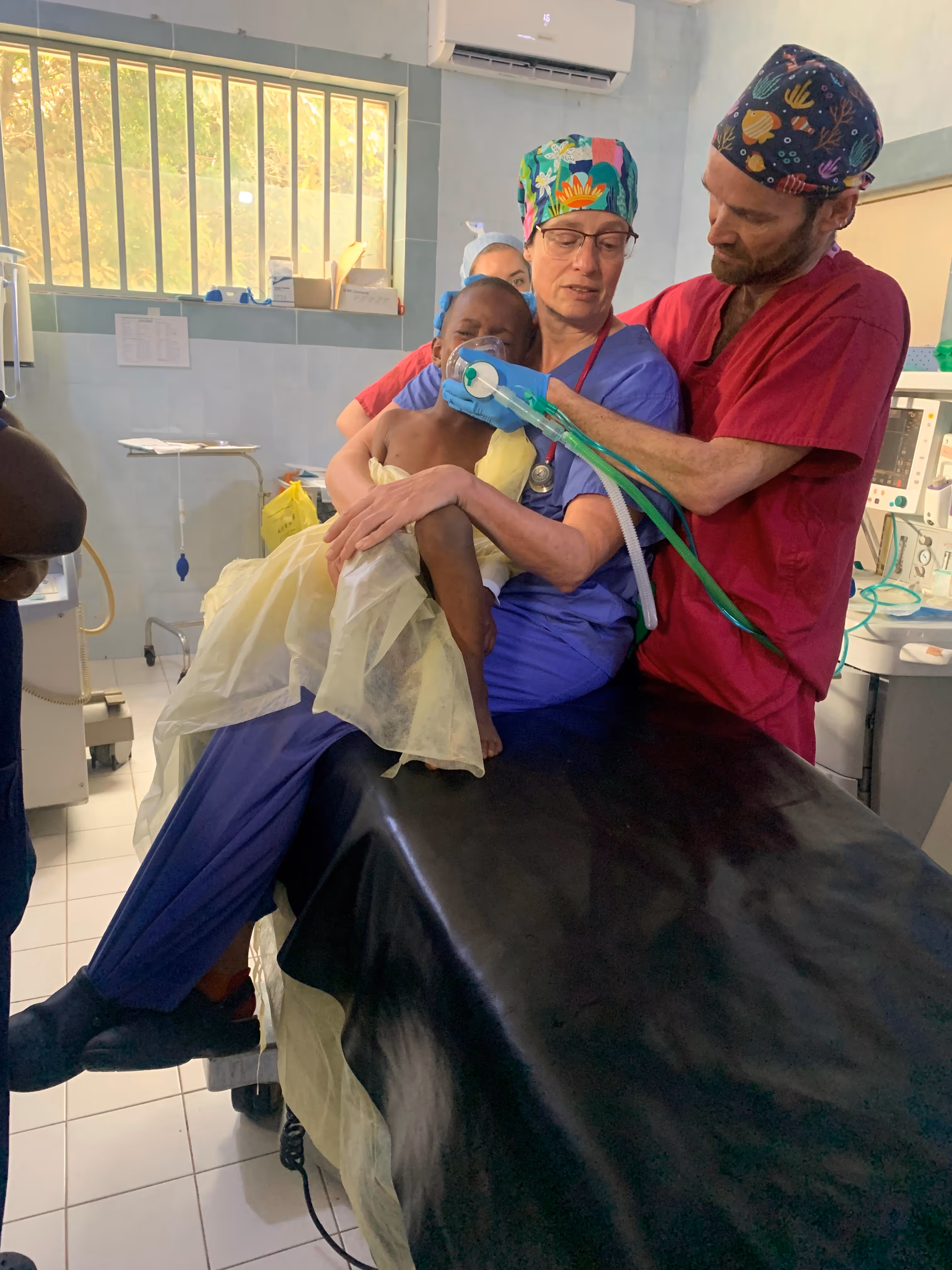 Two medical professionals help a child with a breathing mask in a hospital room.