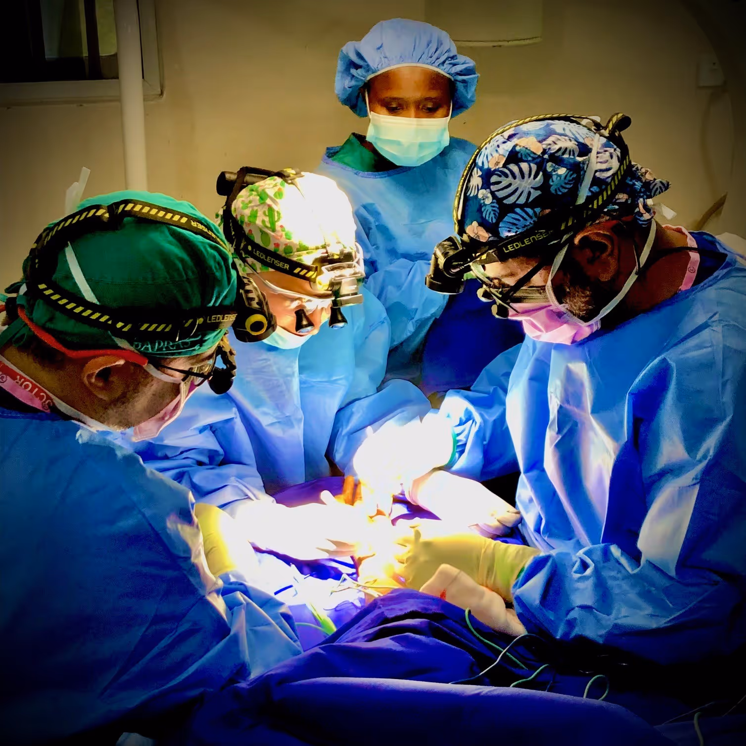 Surgeons in blue scrubs perform surgery under bright lights, with a nurse observing nearby.