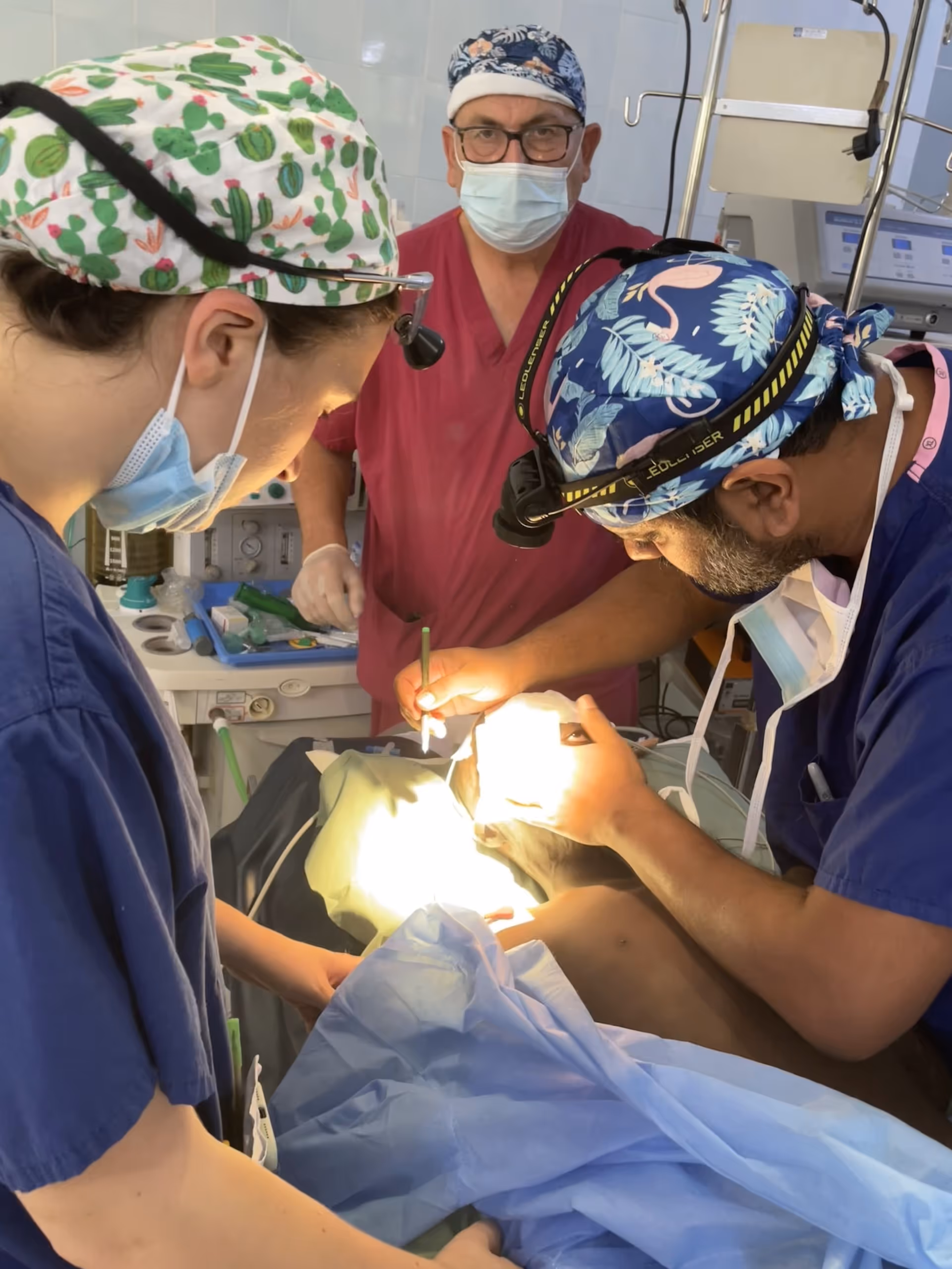 Three surgeons wearing masks and surgical attire perform a procedure on a patient in an operating room.
