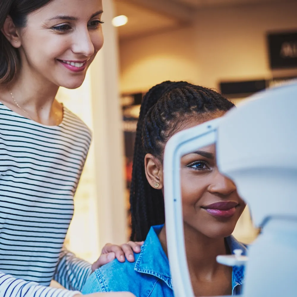 Two people smiling while one looks through an eye exam device