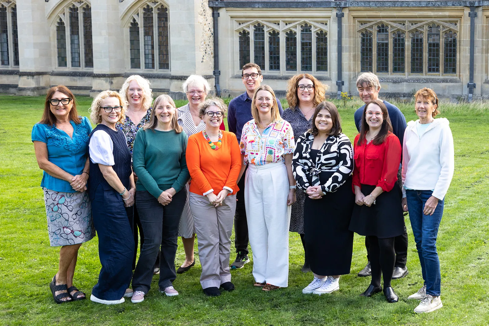 Group photo of diverse team standing on grass in front of historic building
