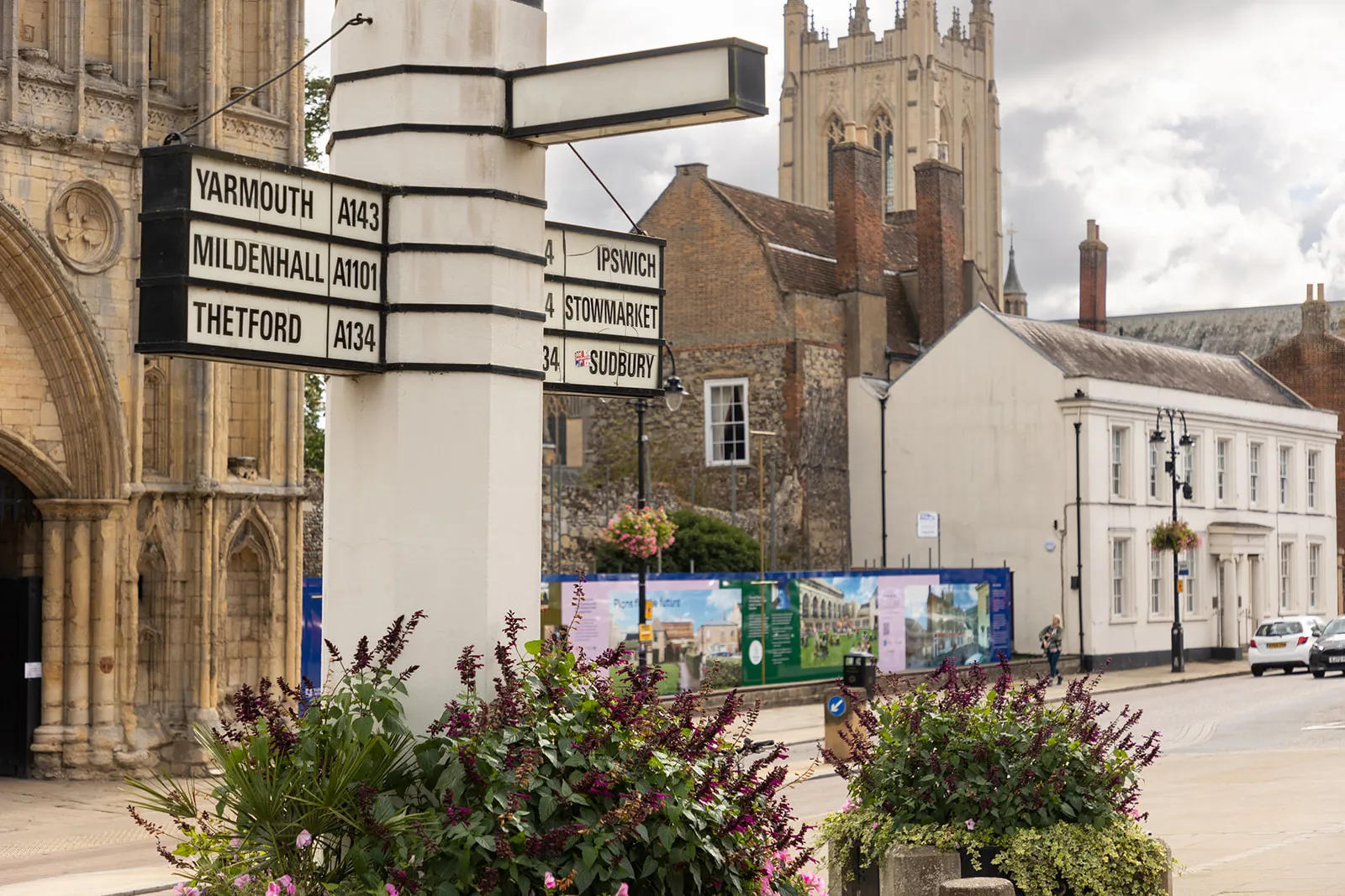 Road sign with directions to Suffolk towns near historic church and buildings