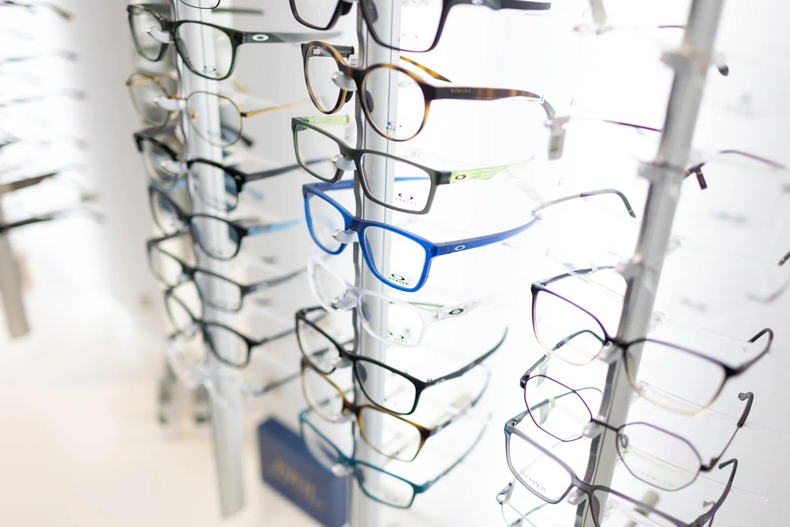 Rows of colorful Oakley eyeglasses displayed on a rack in an optical store