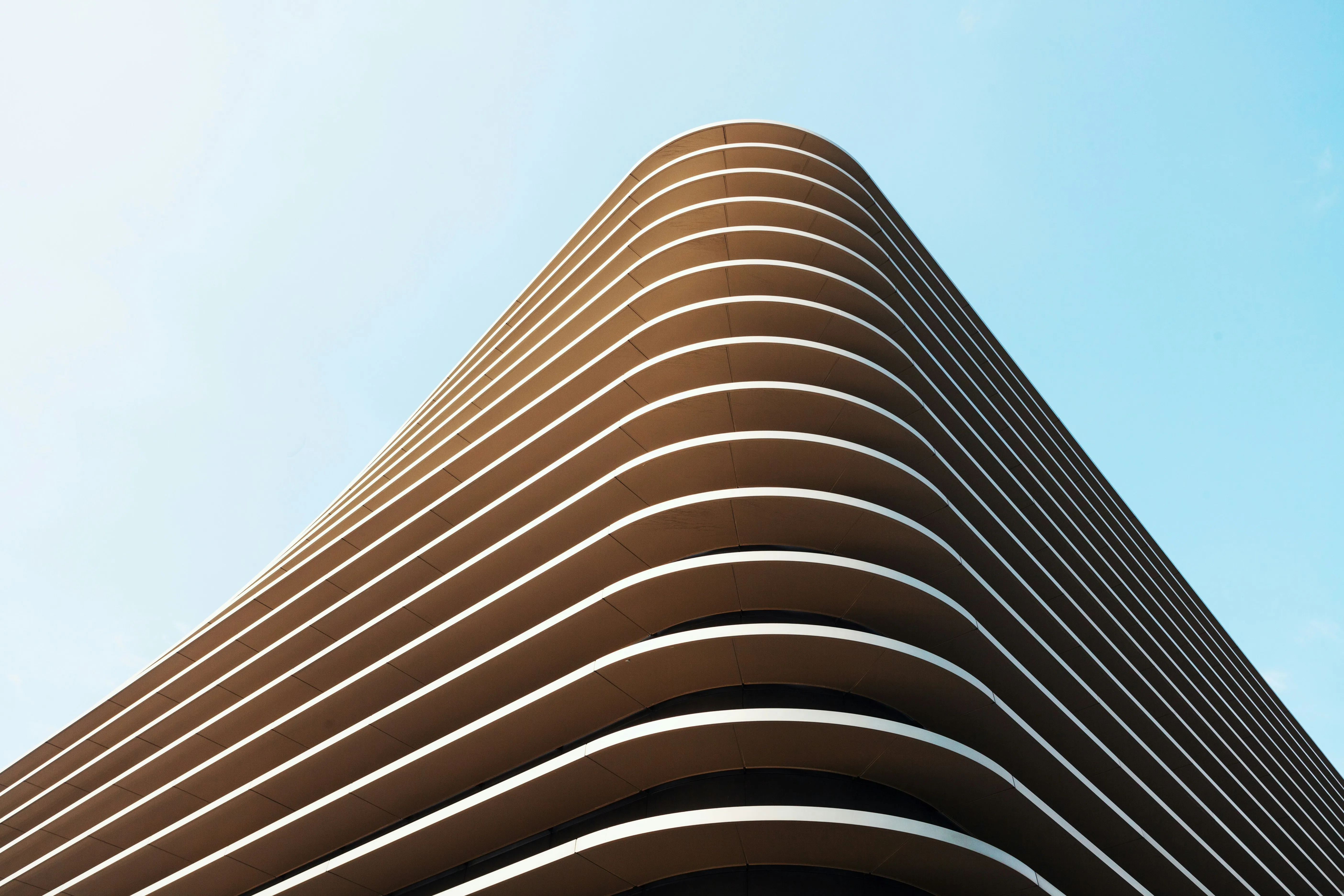 Modern building corner with curved horizontal balconies against a clear blue sky.
