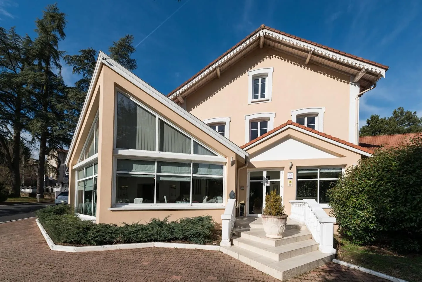 Façade de la bâtisse principale des Cèdres Bleus à Aurec-sur-Loire avec l’entrée de l’établissement et la véranda du restaurant