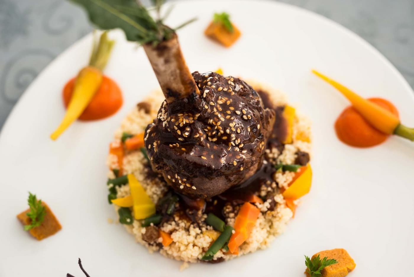 Souris d’agneau confite sur lit de couscous et légumes colorés, sauce aux épices