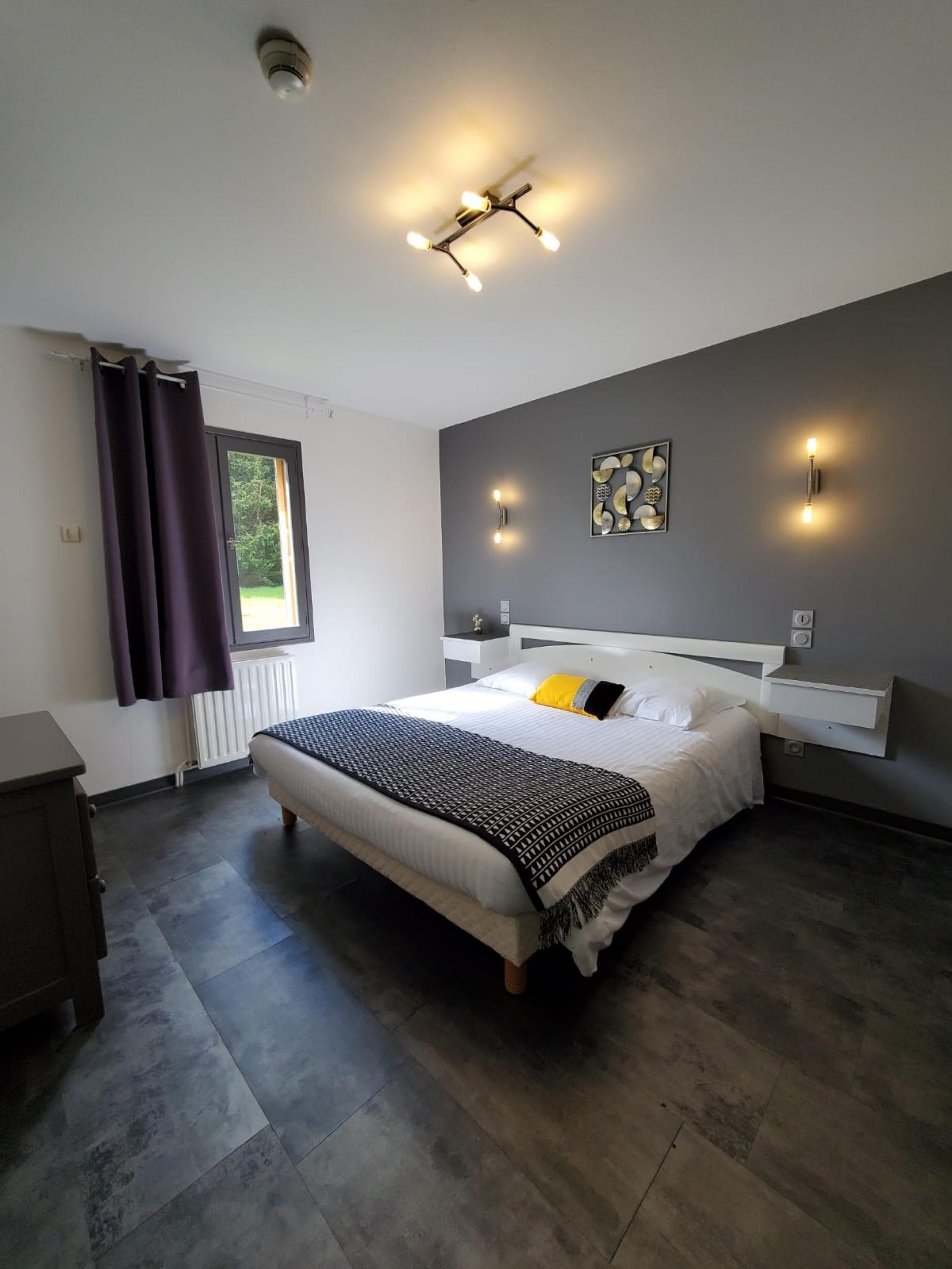 Chambre double moderne avec lit king size, mur gris anthracite, éclairages muraux et décoration sobre