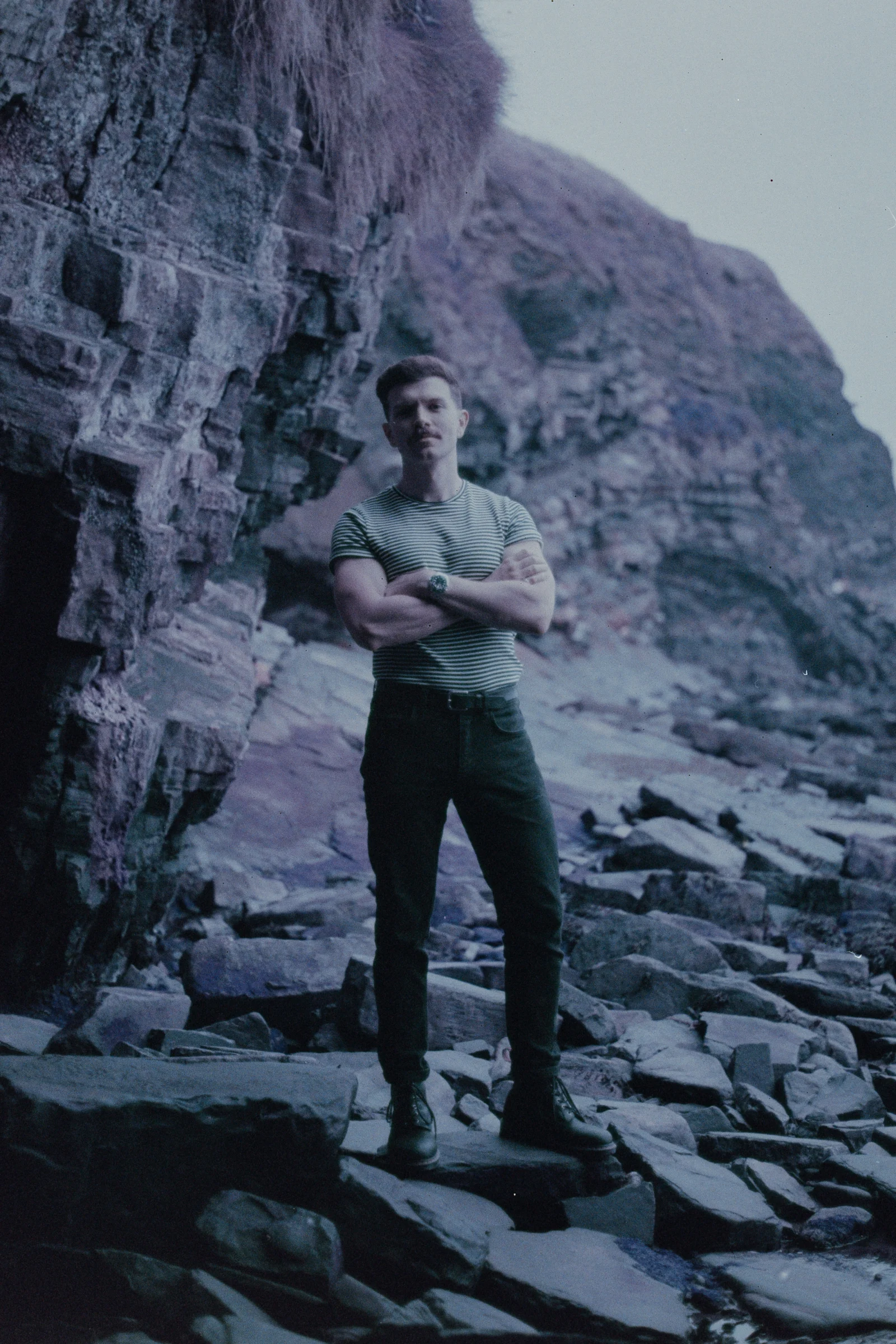 Andrew Gavin standing on a rocky shoreline beneath a cliff