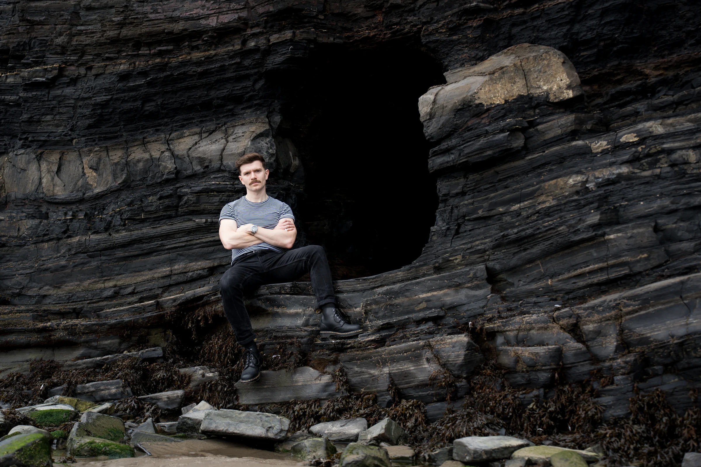 Andrew Gavin sitting beside a sea cave on a rocky shore