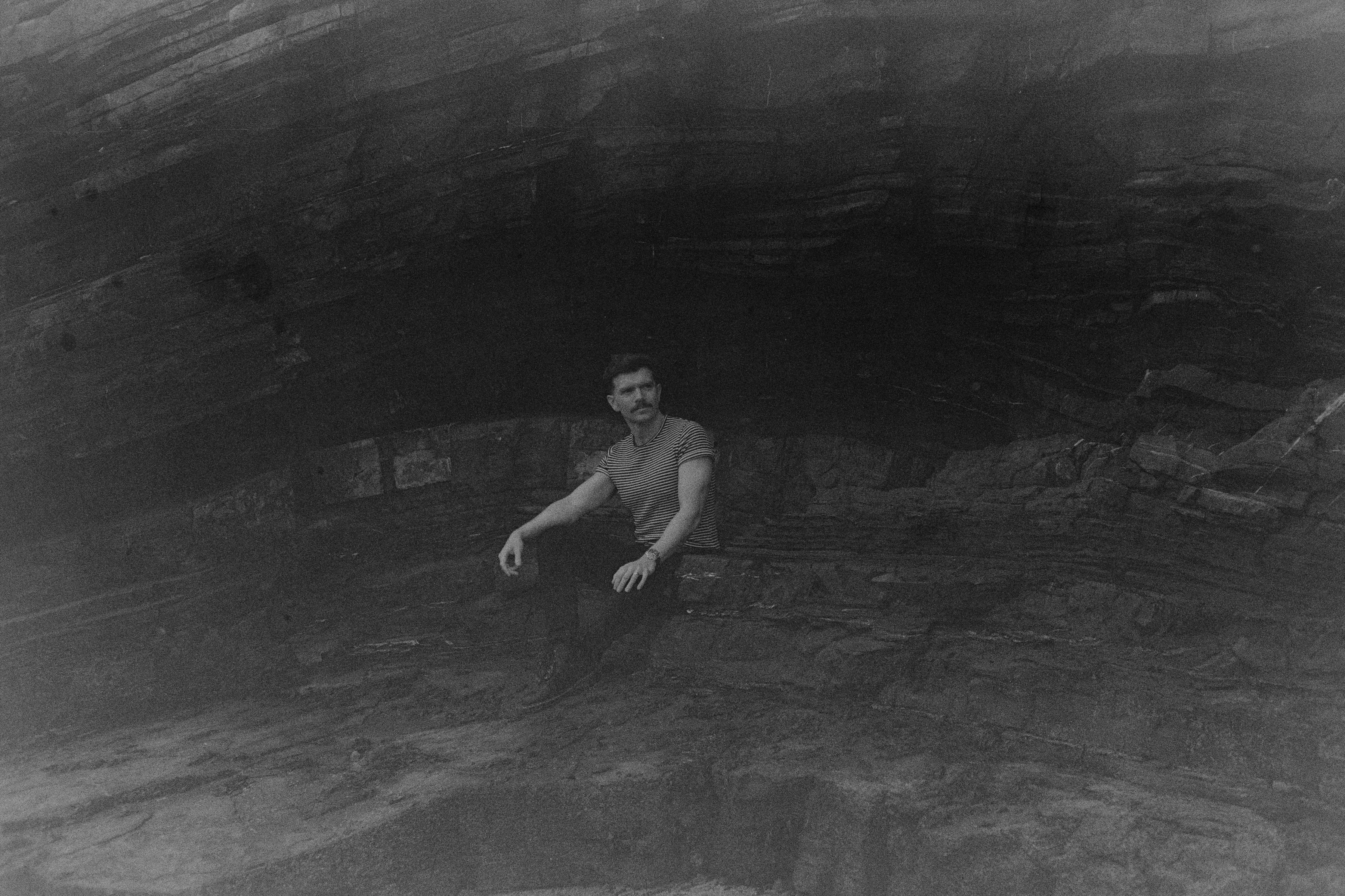 Black and white photo of Andrew Gavin seated inside a sea cave