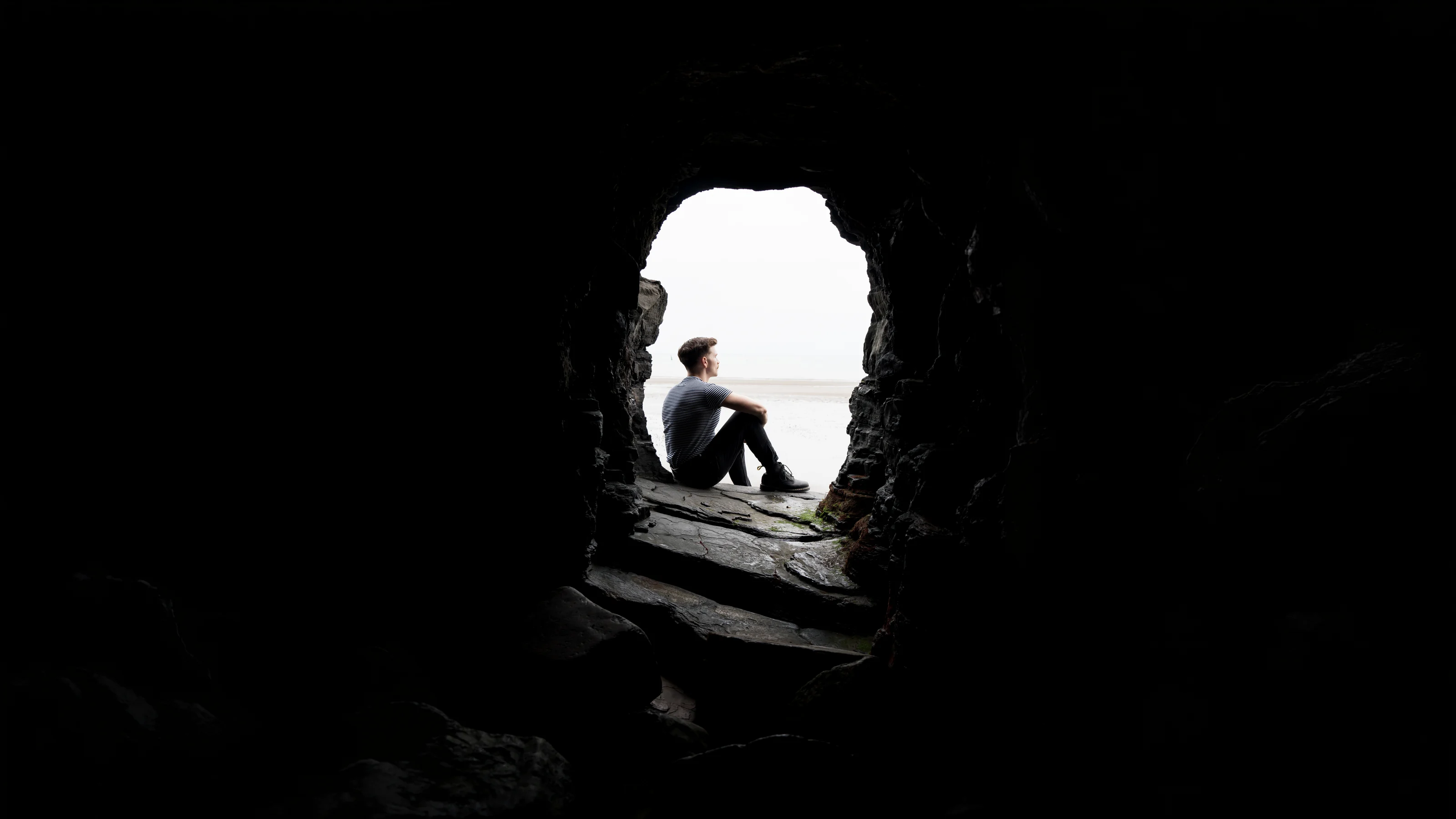 Andrew Gavin seated in the mouth of a sea cave, looking out to the shore