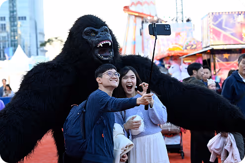 Two people taking a selfie with a person in a large gorilla costume at an outdoor event.