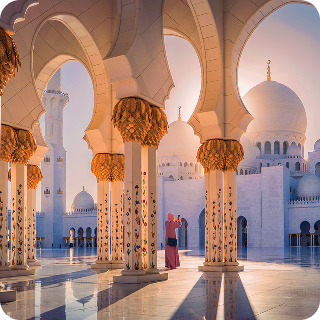 Woman in traditional dress taking photo of Sheikh Zayed Grand Mosque’s ornate columns and domes at sunset.